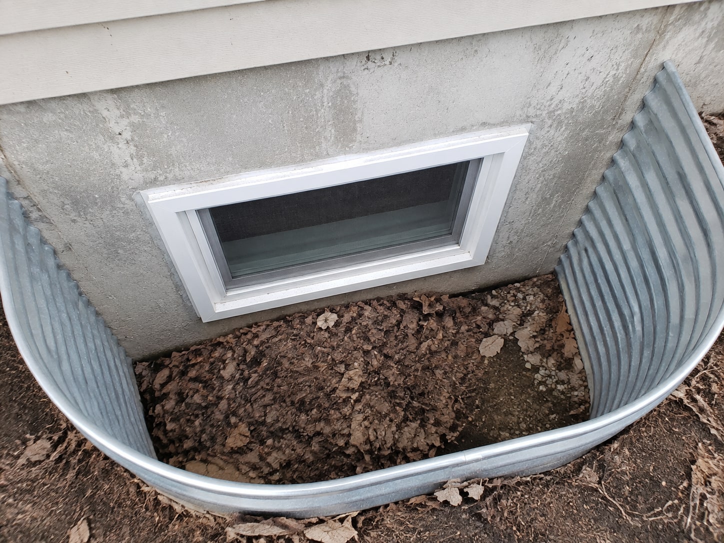 Leaves and soil obscure the base of the lower-level window well.